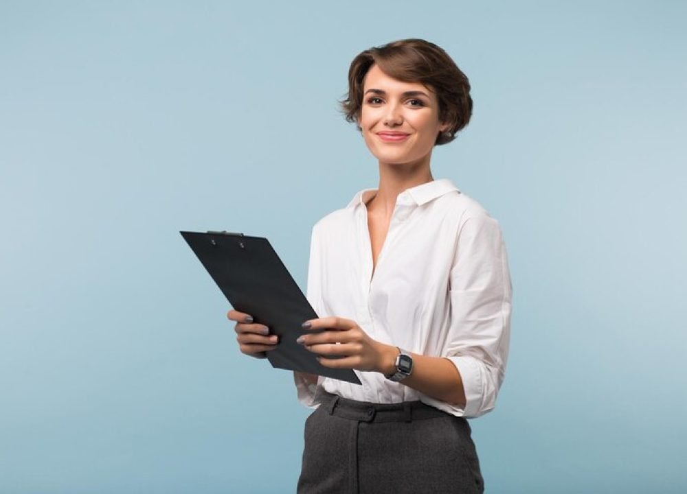 beautiful-business-woman-with-dark-short-hair-white-shirt-holding-black-folder-hands-while-joyfully-looking-camera-blue-background_574295-3492